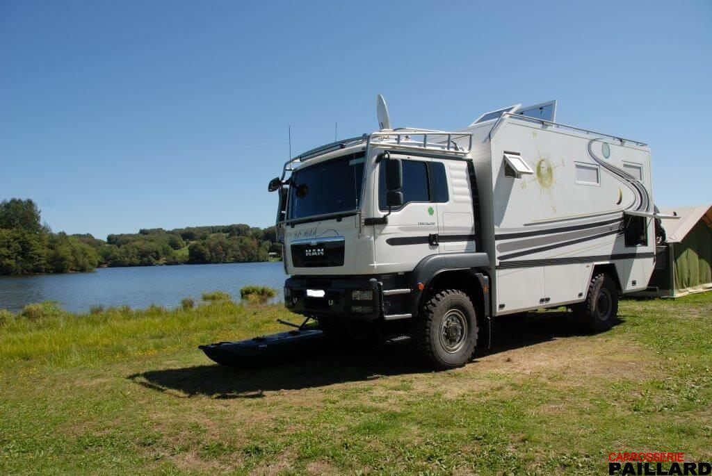 Camping-car MAN 4×4 blanc stationné au bord d’un plan d’eau